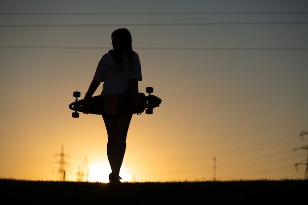 Menina olha o pôr do sol, segurando um longboard na mão