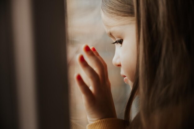 Menina olha pela janela de um prédio alto em uma área de dormir, inclinando o rosto contra o vidro