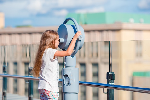 Menina olhando binóculo a moedas no terraço com bela vista