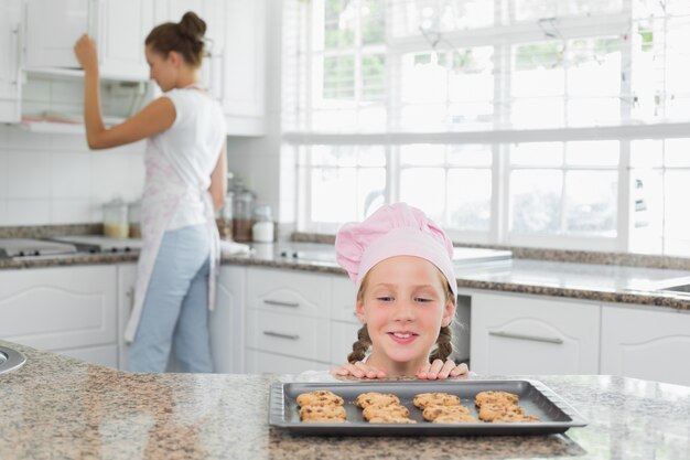 Menina olhando biscoitos recém-preparados com mãe na cozinha