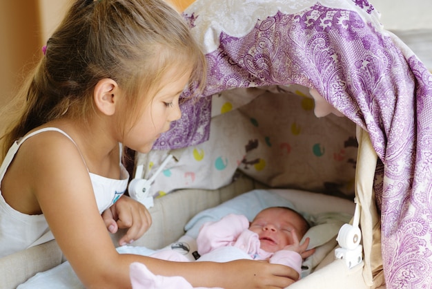 Menina olhando para o bebê recém-nascido no berço