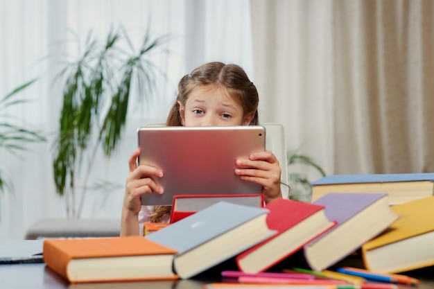 Menina olhando para o tablet PC em uma sala de aula. Livros coloridos à mesa.