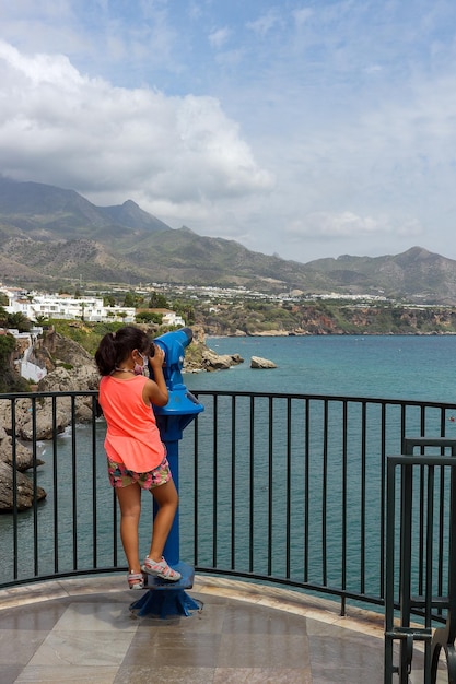 Foto menina olhando pelo telescópio para as vistas da varanda da europa em nerja