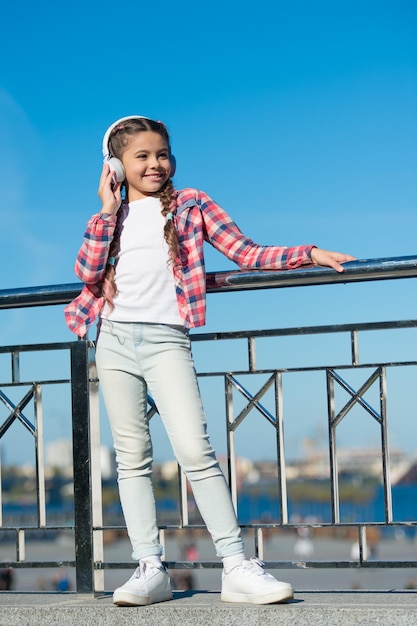 Menina ouve música ao ar livre com fones de ouvido modernos. Fones de ouvido infantis testados e classificados do melhor ao pior. Desfrute de som. Faça seu filho feliz com os fones de ouvido infantis com melhor classificação disponíveis no momento.
