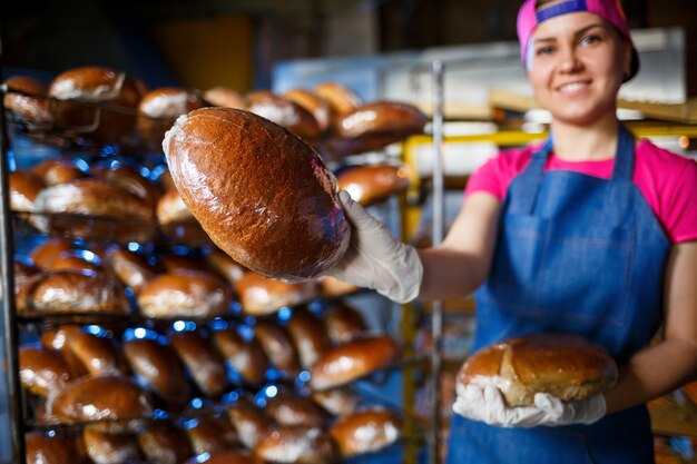 Menina padeiro sorridente no avental segurando o pão e olhando para a câmera. A jovem é uma chef segurando bolos frescos. Uma garota feliz, de aparência europeia, está sorrindo para a padaria.
