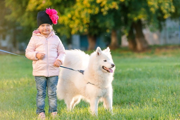 Menina passeando com seu cachorro Samoyed no parque no outono