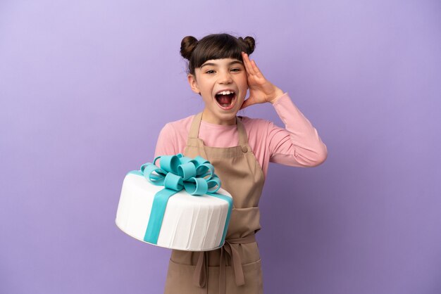 Menina pastelaria segurando um grande bolo isolado em um fundo roxo com expressão de surpresa