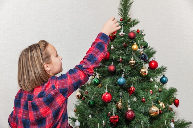 Menina pendura um brinquedo de Natal na árvore de Natal