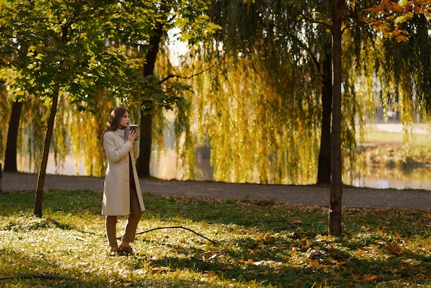Menina pensativa andando com uma xícara de café no parque no outono