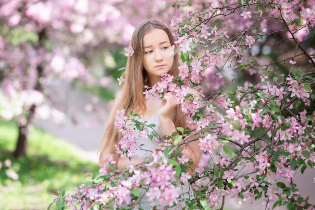 Menina pensativa bonitinha com grinalda de cabelo artesanal na cabeça cheirando flores na flor da primavera