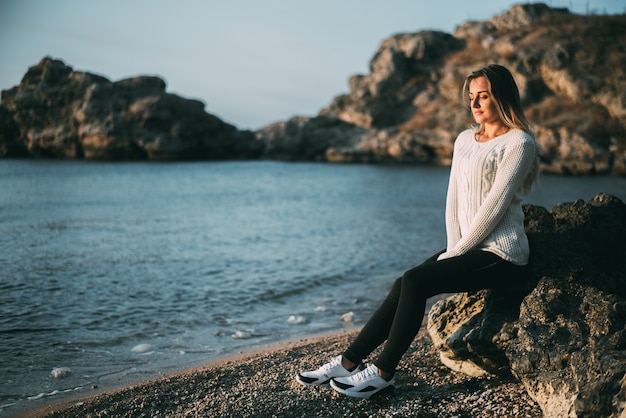 Menina pensativa de suéter e calça no fundo do mar e das rochas