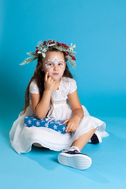 Menina pensativa em um vestido branco, usando uma coroa de flores e tênis sentada no chão