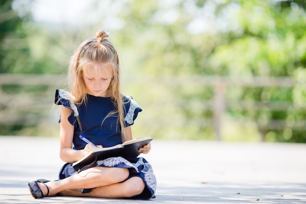 Menina pequena adorável da escola com as notas e os lápis ao ar livre. De volta à escola.