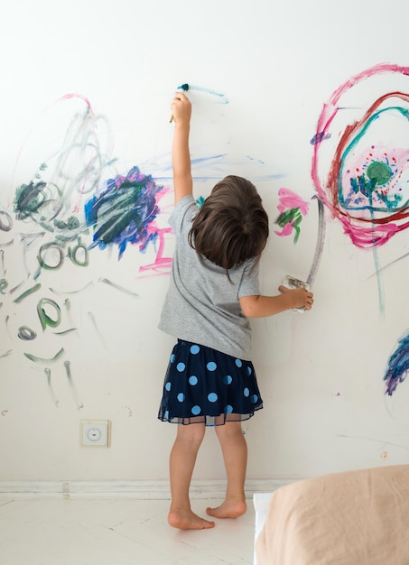 Menina pequena bonito encaracolado da pintura da criança com pinturas cor e parede da escova.