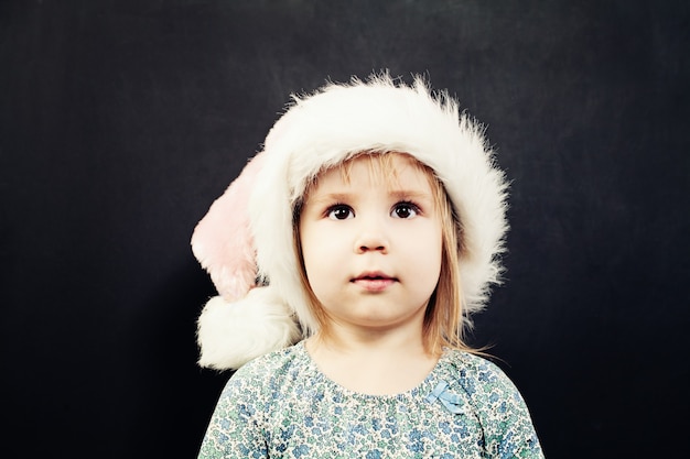 Menina pequena com chapéu de Papai Noel, olhando para cima. Menina fofa de natal
