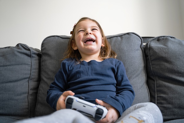 Menina pequena jogando videogame em casa na sala de estar no sofá