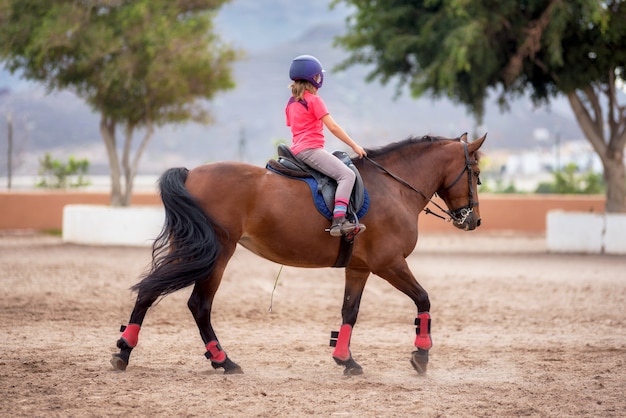 Menina pequena não identificável, montando um cavalo