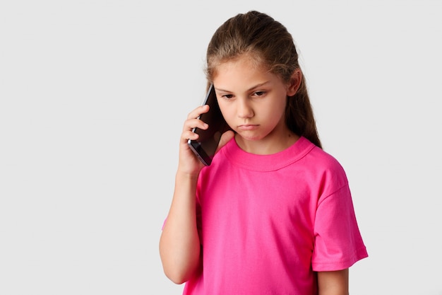 Menina pequena triste falando no celular moderno