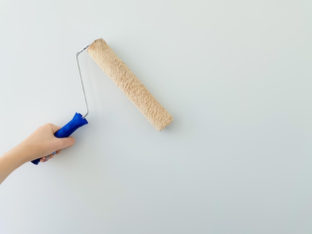 Foto menina pinta a parede com tinta branca mão feminina com rolo de pintura de parede de perto com espaço de cópia