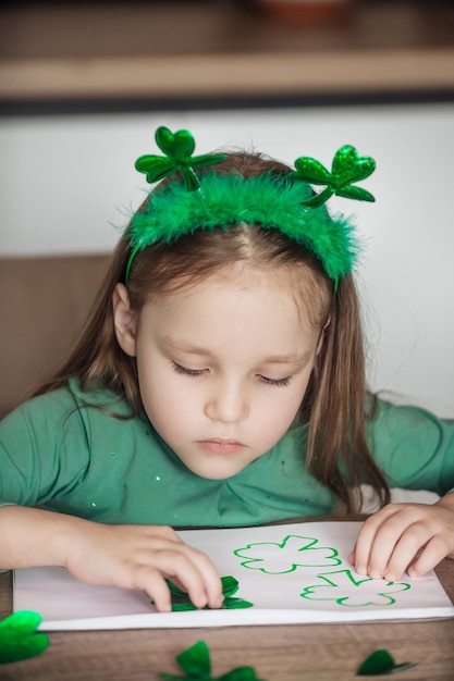 Menina pintando e cortando trevos verdes para o Dia de São Patrício na mesa