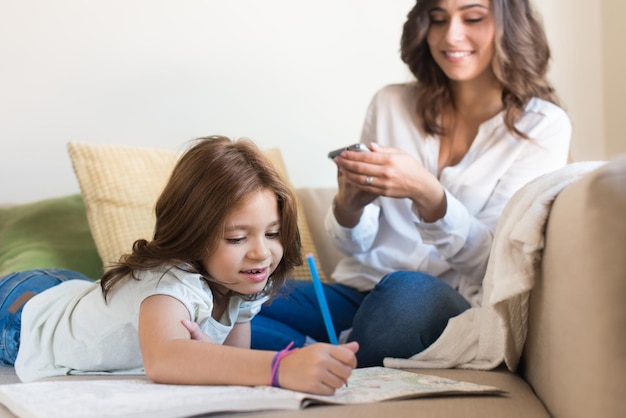 Menina pintando na sala enquanto a mãe está na internet