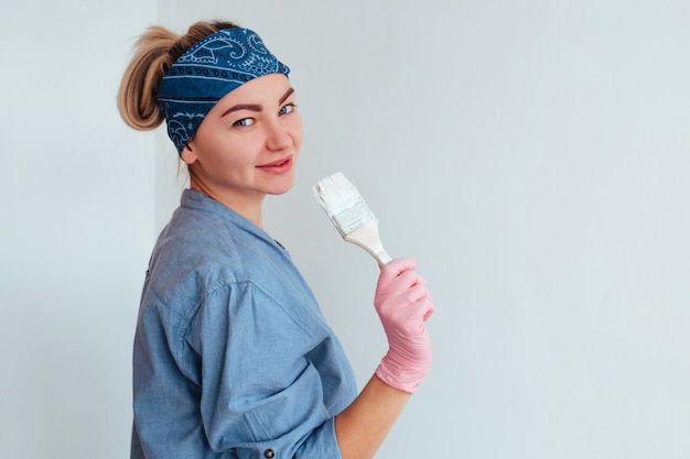 Menina pintora com camisa azul sorrindo pintando a parede