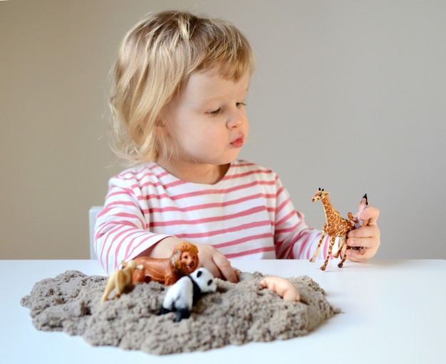 Foto menina plyaying com areia cinética e animais de brinquedo