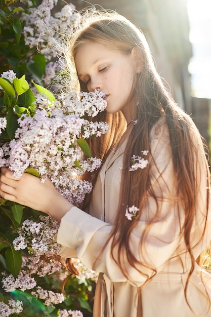 Menina posa em um arbusto de lilases na primavera. retrato romântico de uma criança em flores sob a luz do sol