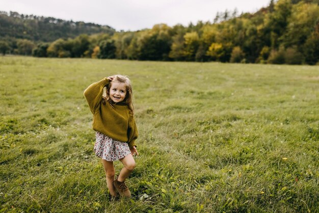 Menina posando e rindo em um campo aberto com grama verde vestindo um vestido e uma camisola