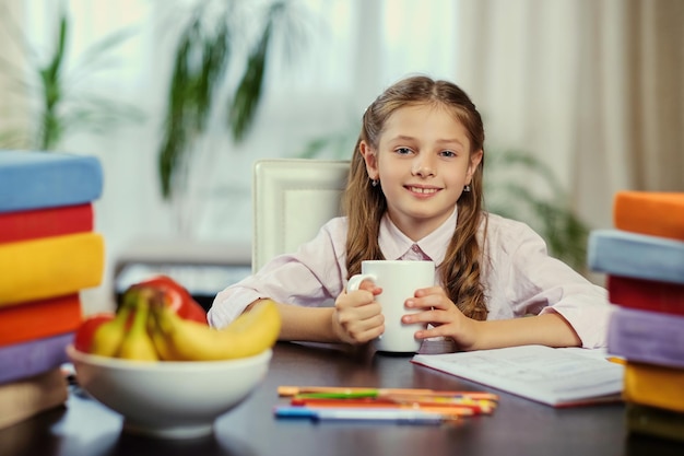 Menina positiva bebe chá da manhã antes de estudar.