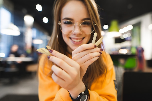 Menina positiva, segurando as batatas fritas na mão