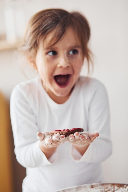 Menina positiva segurando biscoito doce nas mãos na cozinha