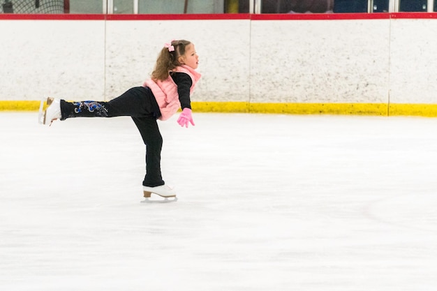 Menina praticando movimentos de patinação artística na pista de gelo coberta