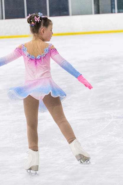 Menina praticando patinação artística em uma pista de gelo coberta.