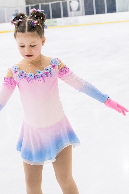 Menina praticando patinação artística em uma pista de gelo coberta.