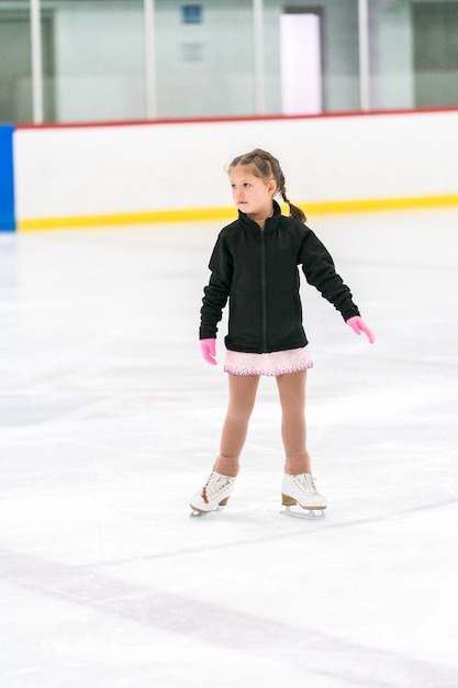 Menina praticando patinação artística em uma pista de patinação no gelo coberta