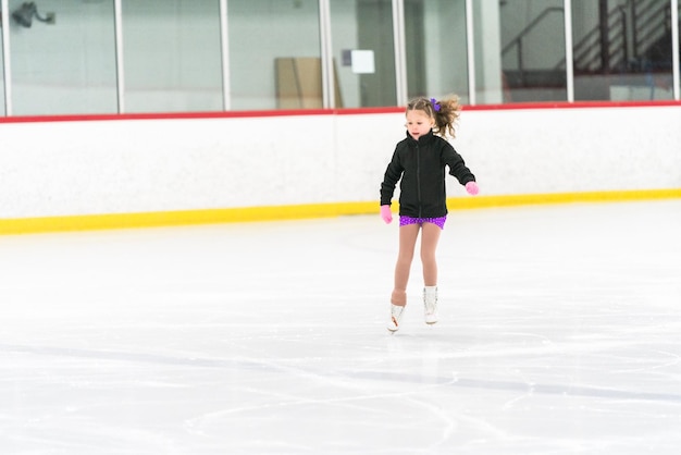 Menina praticando patinação artística em uma pista de patinação no gelo coberta