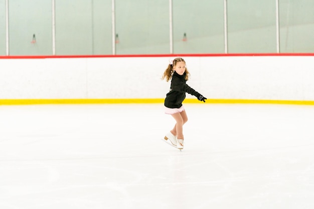 Menina praticando patinação artística em uma pista de patinação no gelo coberta