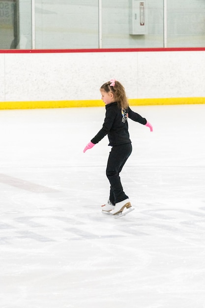Menina praticando patinação artística se move na pista de gelo coberta.