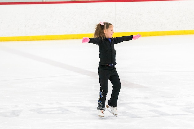 Menina praticando patinação artística se move na pista de gelo coberta.