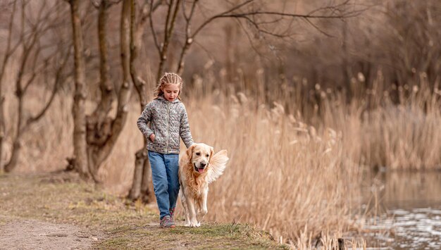 Menina pré-adolescente andando com cachorro golden retriever perto do rio na primavera