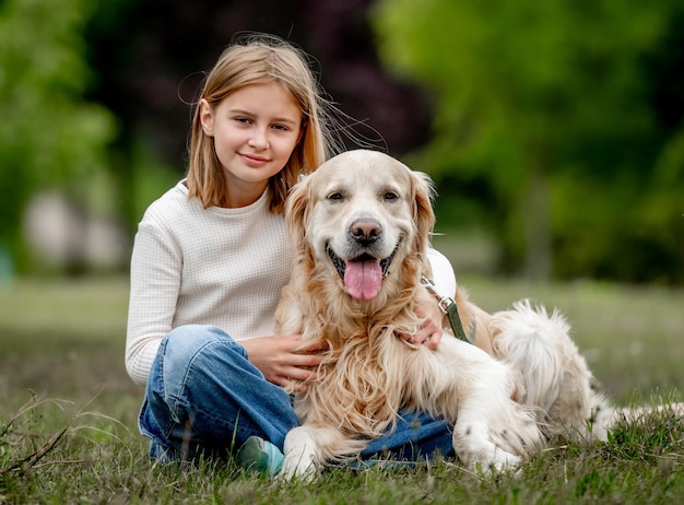 Menina pré-adolescente com cachorro golden retriever sentado na natureza e olhando para trás uma criança fofa abraçando