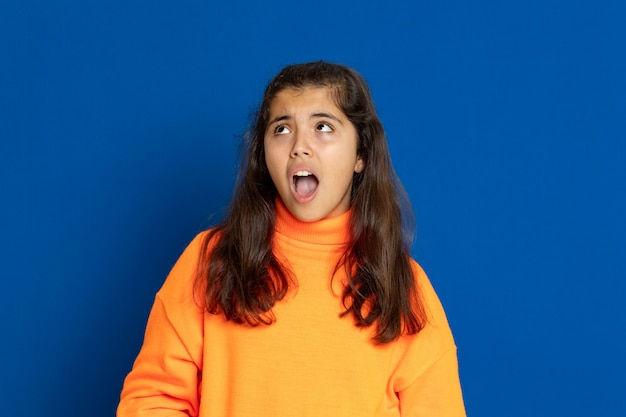 Menina pré-adolescente com camisa amarela, gesticulando sobre parede azul