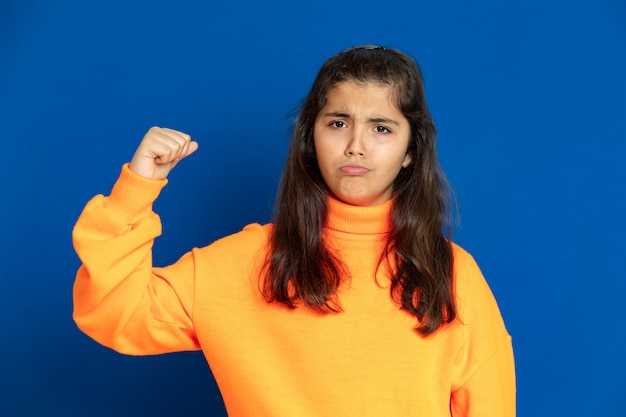 Menina pré-adolescente com camisa amarela, gesticulando sobre parede azul