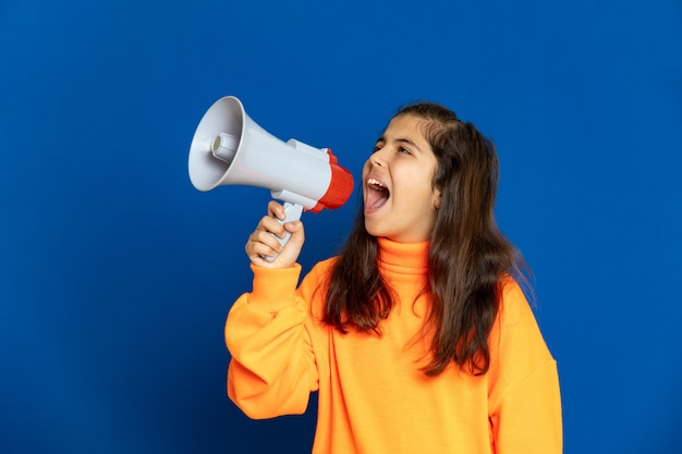 Menina pré-adolescente com camisa amarela, gesticulando sobre parede azul