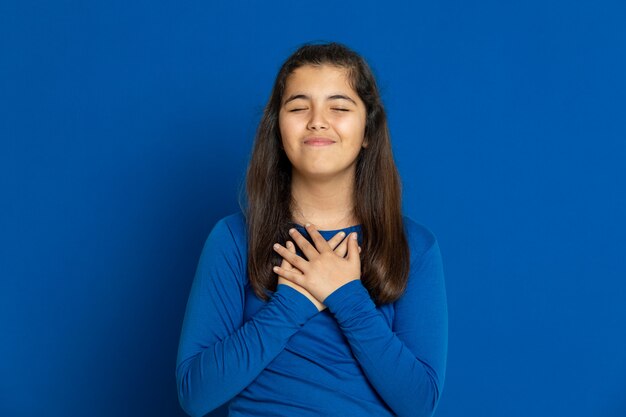 Menina pré-adolescente com camisa azul, gesticulando sobre parede azul