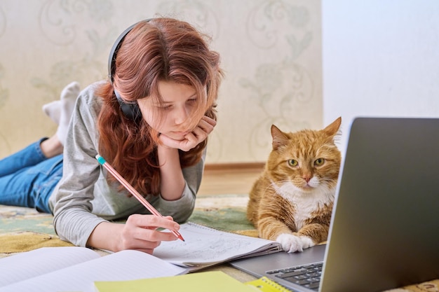 Menina pré-adolescente estudando em casa com gato ruivo usando laptop