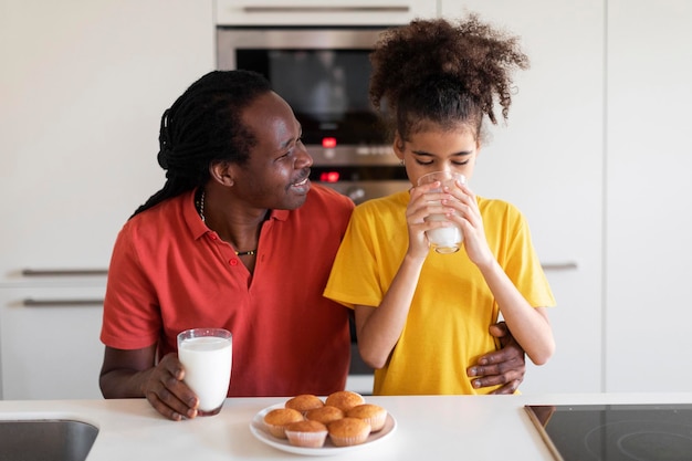 Menina pré-adolescente negra e seu pai comendo lanches juntos na cozinha