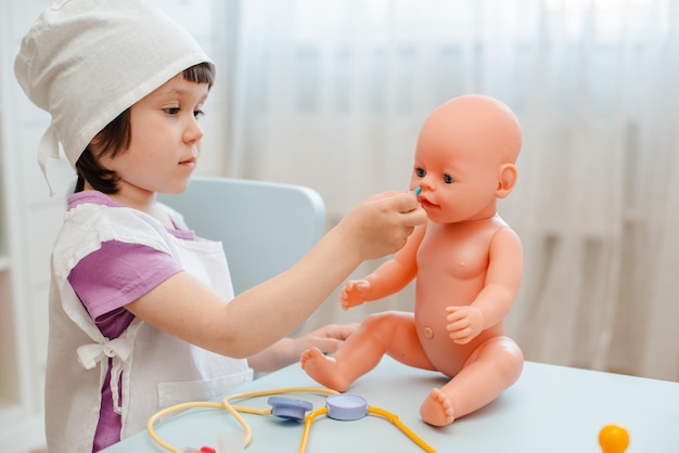 Menina pré-escolar de 3 anos brincando de médico com boneca A criança faz um brinquedo de injeção