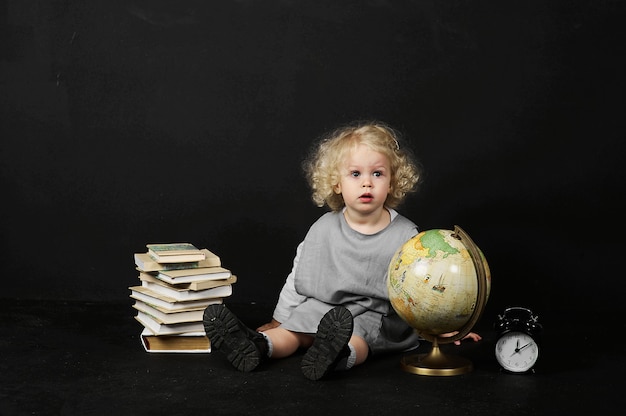 Menina pré-escolar feliz com livros, globo e relógio em um fundo preto